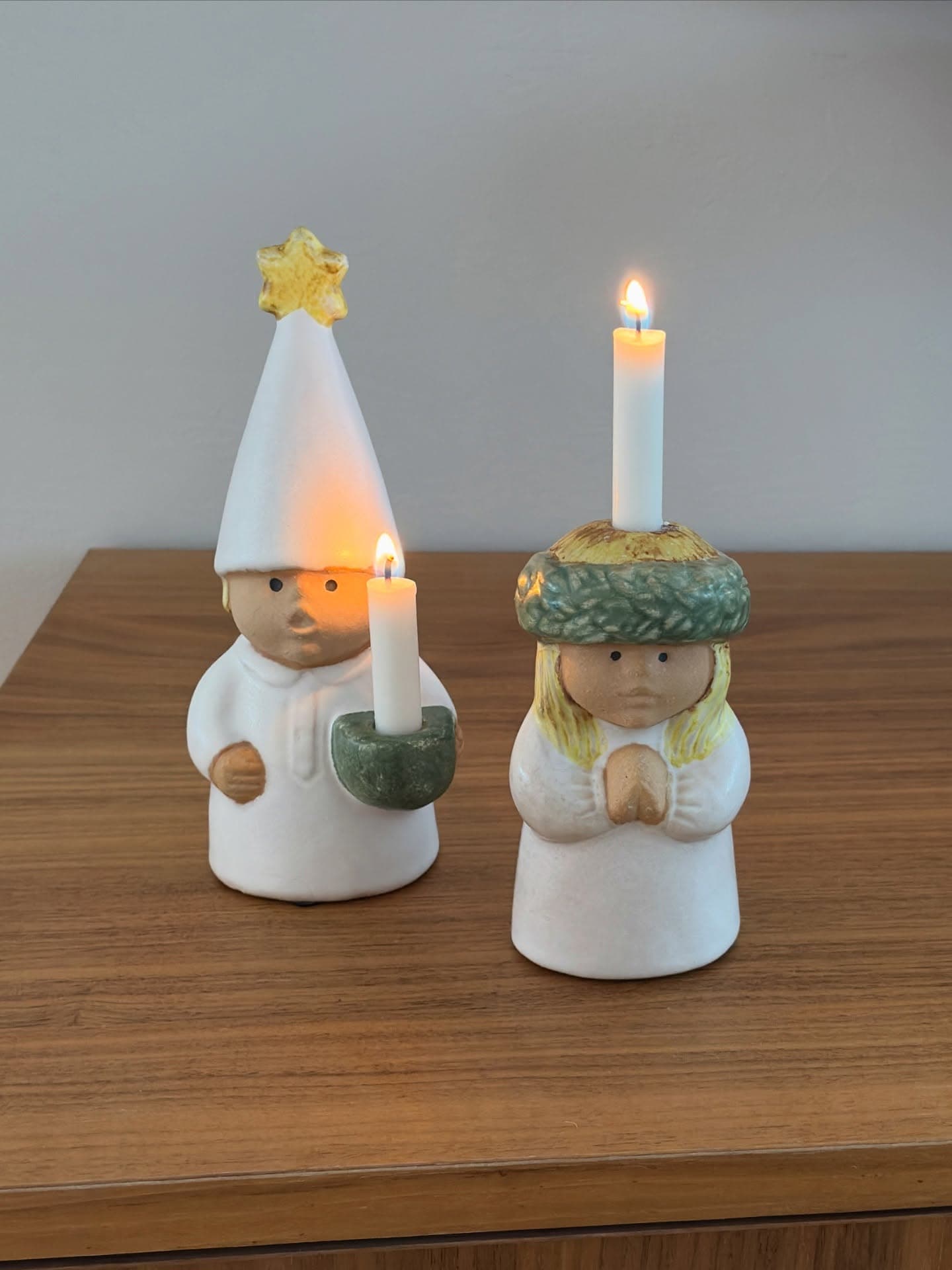 Two lit Swedish Lucia candle holders, boy with star hat and girl with wreath.
