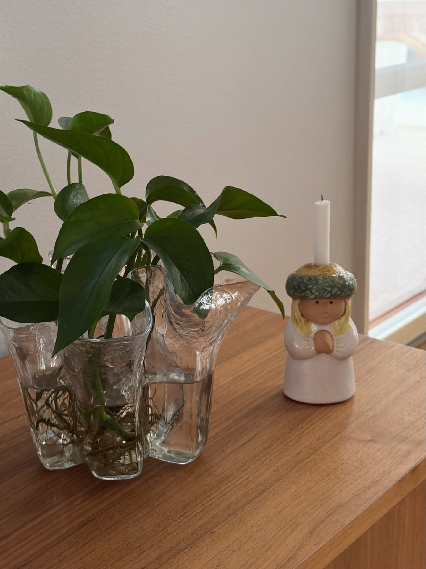 Indoor scene with green pothos in glass vases and candle in praying angel holder.