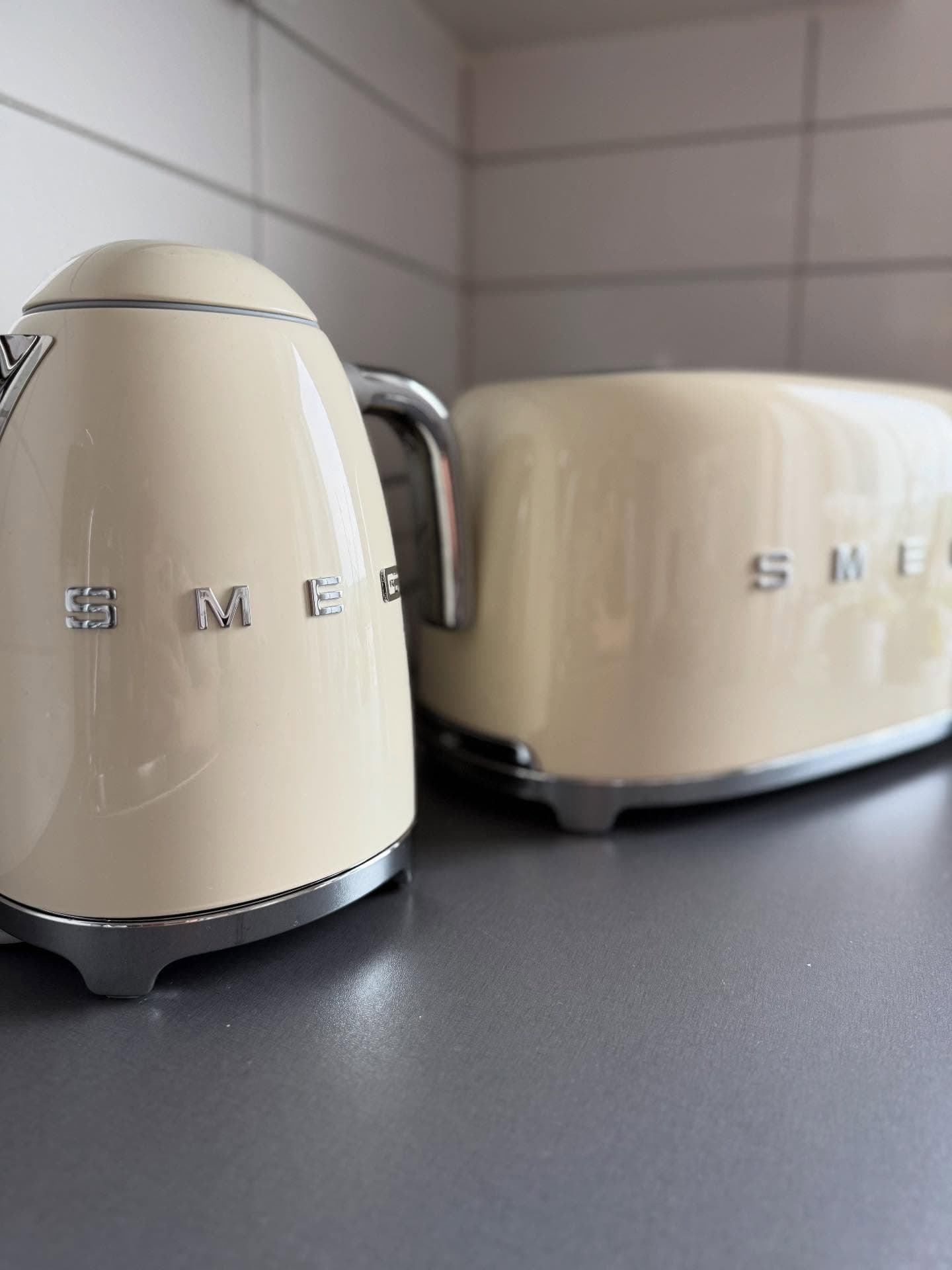 Close-up of a cream-colored Smeg kettle and toaster on a gray countertop.