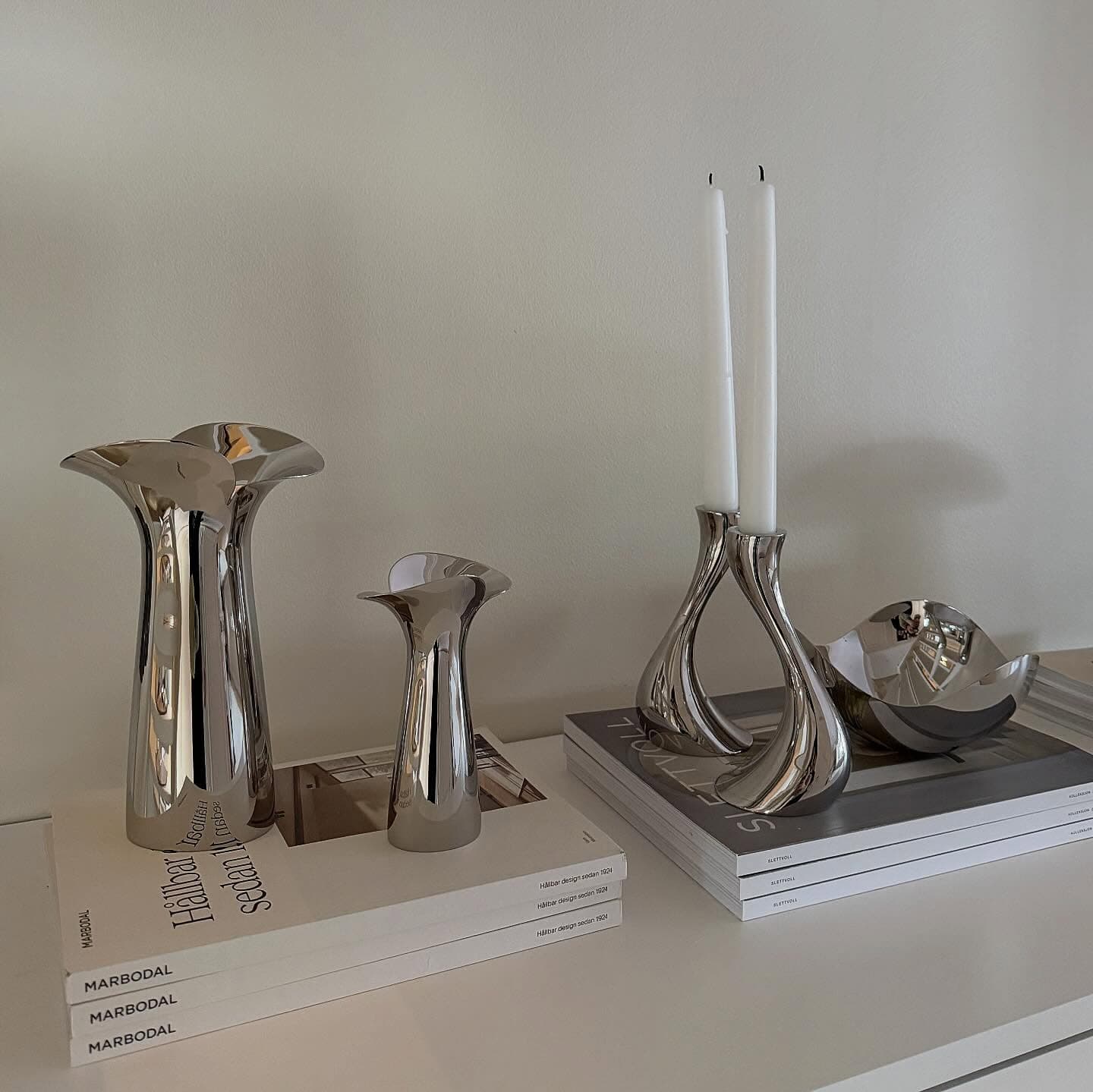 Silver vases, candleholders with candles, and a bowl on books.